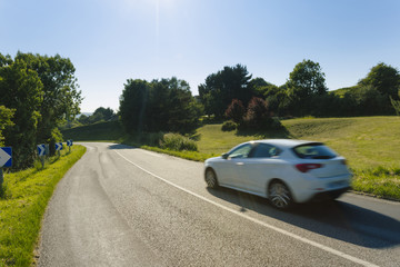Asphalt road with cars passing through the fields in the region of Normandy, France. Landscape in spring day.