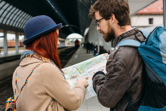 Picture showing young couple sightseeing with map. Boyfriend with backpack, red hair girlfriend in blue hat. People holding touristic map. Travel Concept