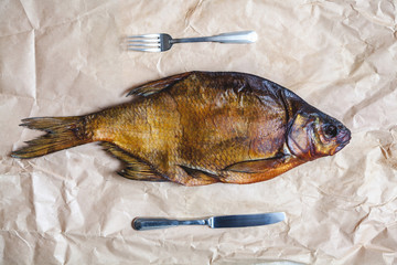 Great smoked fish, knife and fork on parchment paper.