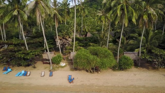 Chais lounge chairs on the beach are ready for tourists under swaying palm trees on the lush tropical island of Koh Tonsay, Rabbit Island, in Cambodia.