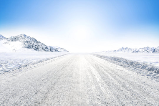 Winter Background Of Foreground Of Road Covered With Snow And Ice. In The Background, The Arctic Landscape Of The Mountains With The Beautiful Blue Sky.