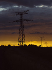 High voltage power lines and transmission towers at sunset. Poles and overhead power lines silhouettes in the dusk. Electricity generation and distribution. Electric power industry and nature concept