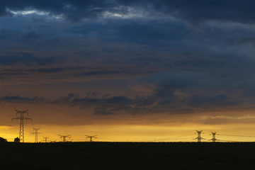 High voltage power lines and transmission towers at sunset. Poles and overhead power lines silhouettes in the dusk. Electricity generation and distribution. Electric power industry and nature concept