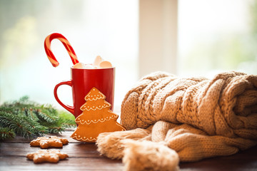 Christmas gingerbread, candy, coffee with marshmallows in red cup, knitted scarf, cones  and christmas tree branches on wooden table on window background. Xmas holidays background, winter home cozy