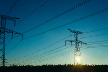 High voltage power lines and transmission towers with sunbeams in the blue sky in Normandy, France. Countryside landscape. Electricity generation and distribution. Electric power industry and nature
