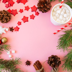 Christmas background with copy space, fir tree branches, hot chocolate with marshmallows, anise, cinnamon, pine cones, red star garland. Pink backdrop.