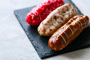 Set of assorted eclairs served on a slate board on a white stone background.