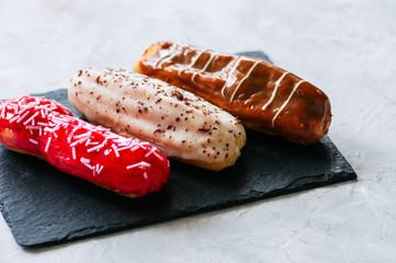 Set of assorted eclairs served on a slate board on a white stone background.