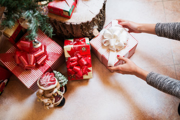 Close up of woman hands putting down a gift box under a Christmas tree.