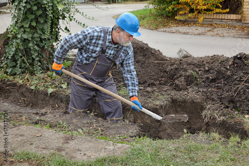 "Construction worker digging trench using shovel, hole for ...