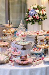 Delicious wedding reception candy bar dessert table full with cakes and sweets and a flower vase with hydrangeas on the background of an exquisite restaurant.