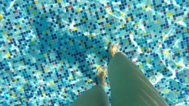 Female legs walking along bottom of pool. Point of view of woman stepping at swimming pool during summer vacation. POV Close up Slow motion