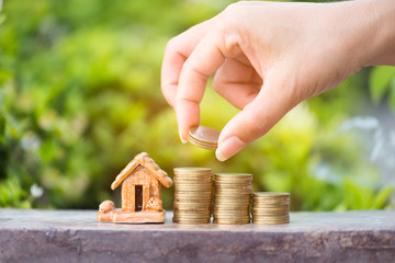 close up of woman putting money golden coin like stack  with house,Saving money. Female hand stack coins to shown concept of growing business and wealthy.