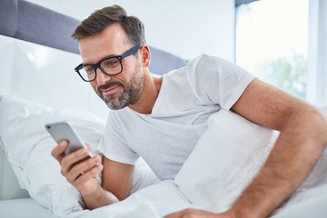 Handsome man using phone in bed at the morning