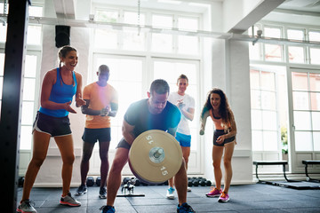 Fit man lifting weights with friends clapping in the background