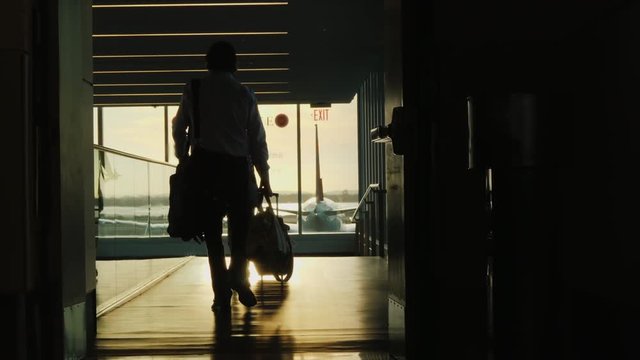 Silhouette of businessman with bag, goes on boarding the plane. In the rays of the setting sun. Back view
