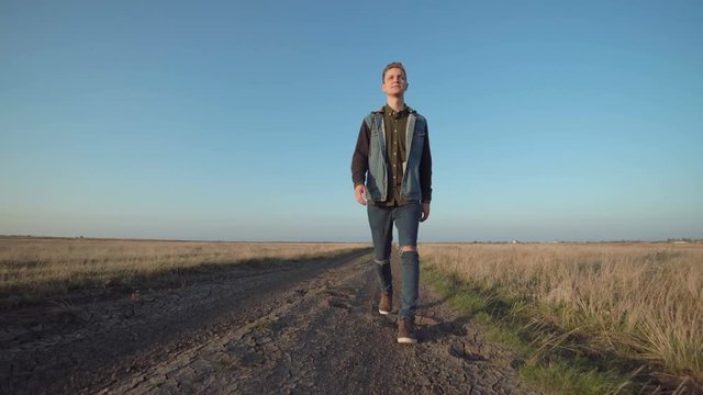 Front view of young lone man walking away down a rural road in a low angle view in a conceptual motion clip