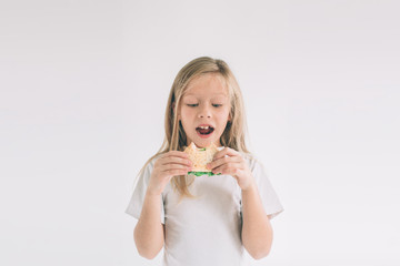 Child holding a piece of hamburger. Kid eats fast food. not helpful food. very hungry baby. Girl isolated on white background