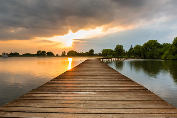 Wooden pier, bridge over lake at dramatic sunset with stormy clouds. Kuchyna, Slovakia. Landscape.