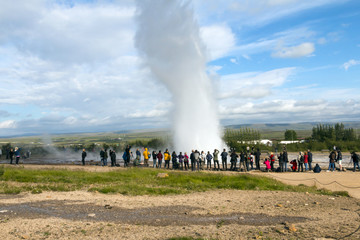 Obraz premium Iceland landscape - geyser valley - hot steaming geothermal sources, people walking and watching geologic features. Geyser eruption. People watching.