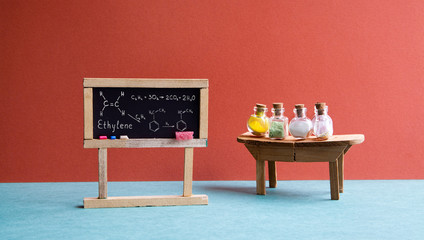 Chemistry lesson classroom laboratory. Black chalkboard with molecular formula ethylene, wooden table and chemical reagent glass bottles. Bright red wall college interior