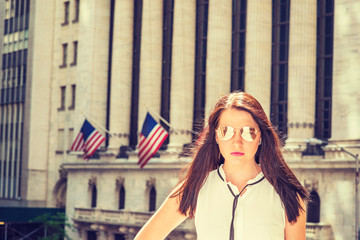 American Woman traveling in New York in hot summer. Lady wearing white collarless sleeveless shirt, mirror sunglasses, standing by vintage building with American flags. Instagram filtered effect..