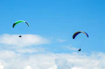 Two paragliders flying in the blue sky against the background of clouds. Paragliding in the sky on a sunny day.