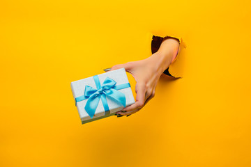 close-up of female hand holding a present through a torn paper, isolated