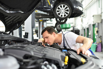 Closeup: Automechaniker kontrolliert Motor eines Fahrzeuges in der Autowerkstatt // Car mechanic inspects the engine of a vehicle in the workshop