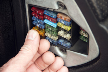 The man presses his finger on the electric fuse in the car to insert it into place.