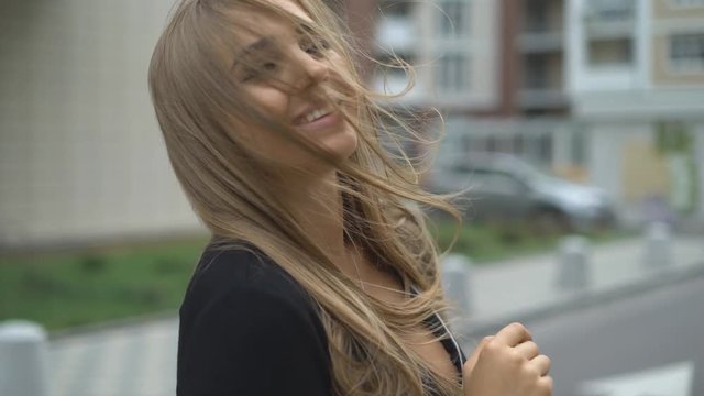 attractive girl smiling at the camera. the woman is dressed in a strict black business dress. a major party. the wind blows the girl's hair. 4k