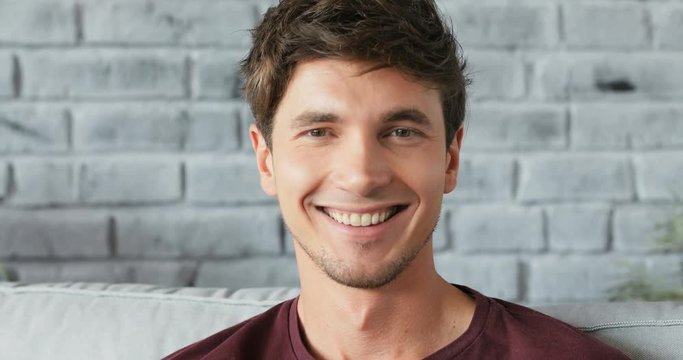 Closeup portrait face young attractive man sitting on the couch looking at the camera smiling satisfaction man casual handsome happy guy leisure relax rest Shot on RED EPIC camera Slow Motion