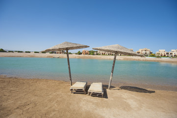 Pair of sun loungers on remote tropical beach with umbrellas