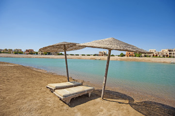 Pair of sun loungers on remote tropical beach with umbrellas