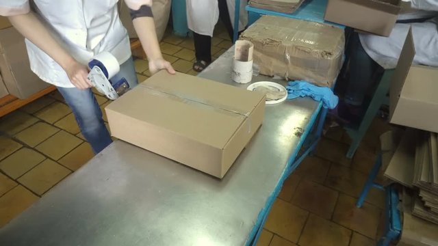 Woman hands holding packing machine and sealing cardboard boxes with adgesive tape