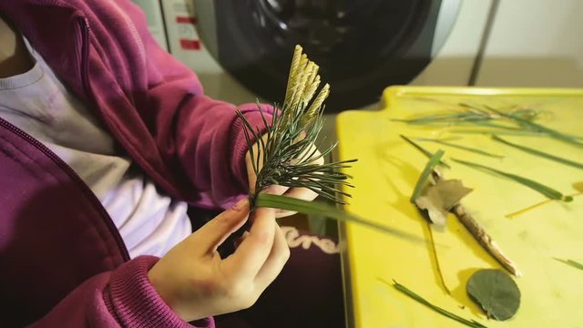 Little girl playing and making decorations out of dry plants. Tying up diferent kind of branches and leaves with grass. Learning hands crafts through playing. Filmed in slow motion hd.