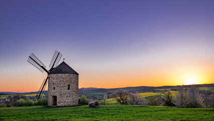 sunset over the countryside with old mill on the left and lot of negative space in the sky