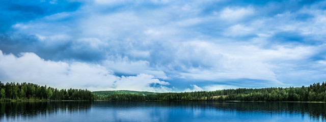 Fototapeta na wymiar Peaceful landscape with lake, forest and spectacular, blue, cloudy sky reflecting in the water