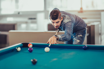 Handsome young man playing pool in pub