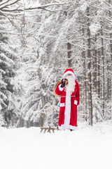 Santa Claus walking through a white winter landscape with a sledge and a bag of gifts