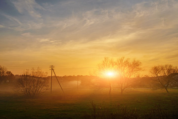 Obraz premium An landscape of autumn and foggy countryside greenfield with village on a background at sunset