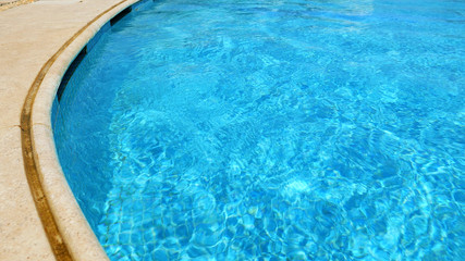 Fototapeta na wymiar Blue water in swimming pool. Waves and patches of sunlight appears on the bottom of the pool. Glares blinks and reflections on clear water.