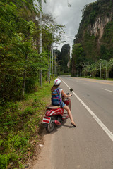 tourist woman sitting on classic scooter against the background of the mountains of Krabi Province, Thailand.