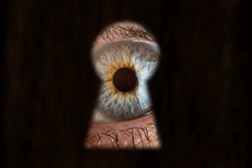Male blue eye looking through the keyhole. Concept of voyeurism, curiosity, Stalker, surveillance...