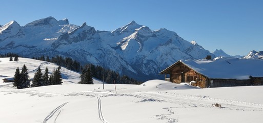 Old timber hut and snow covered mountain Range. Mountains Schlauchhorn and Oldenhorn. Winter scene near Gstaad, Switzerland.