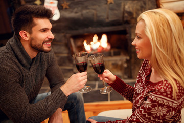 woman and man toasting delicious red wine at romantic fireplace.
