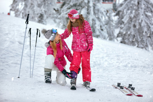 Skiing, winter fun-smiling mother preparing for skiing daughter