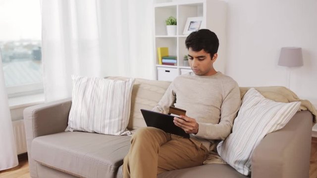 man with tablet pc and credit card on sofa at home