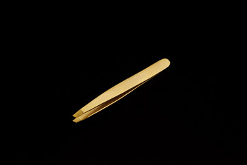 Close up isolated gold tweezers on black background 