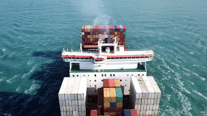Huge large mega ULCV container ship sails on open water fully loaded with containers and cargo - aerial view